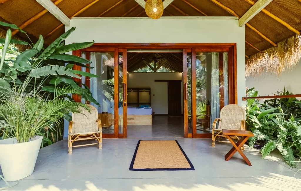 A private room in our Hiriketiya camp, with 2 chairs on the balcony, a plant and a glass sliding door leading into the room.