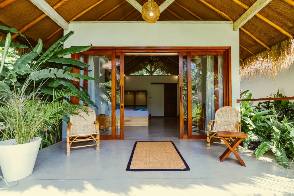 A private room in our Hiriketiya camp, with 2 chairs on the balcony, a plant and a glass sliding door leading into the room.