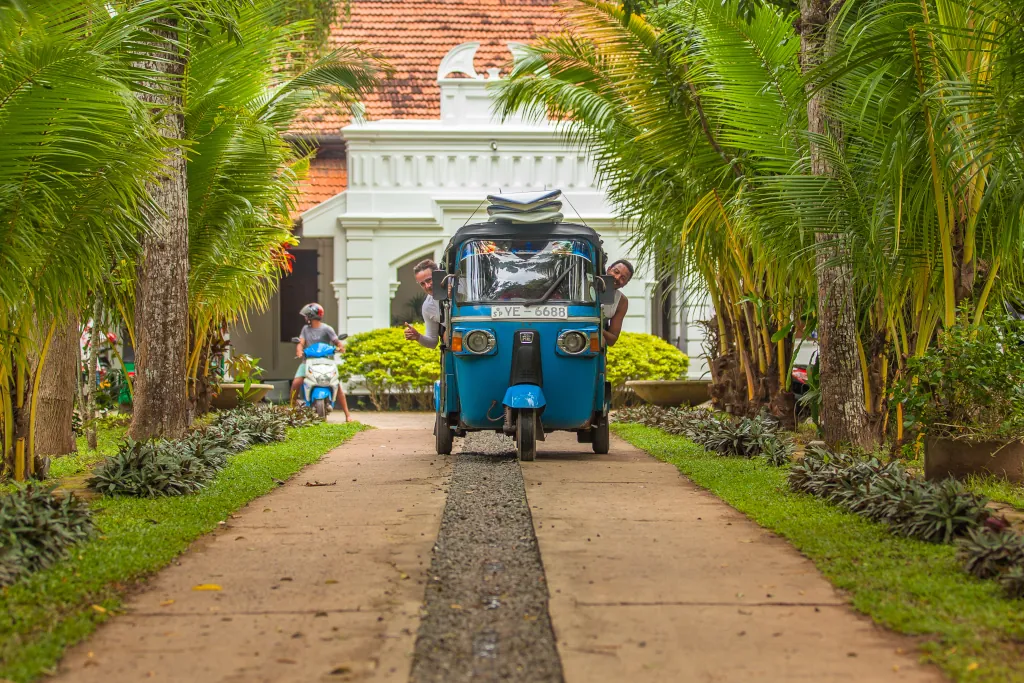 2 men in a tuk tuk with surfboards on the roof
