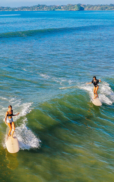SURFER GIRLS SHARING A WAVE IN SRI LANKA